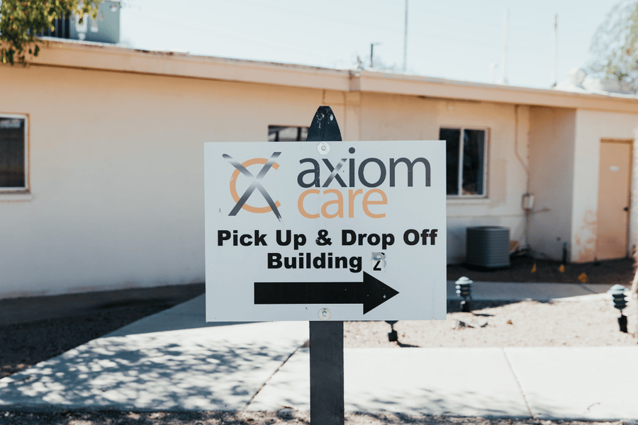 Directional sign outside Axiom Care’s facility, guiding visitors to the Pick Up & Drop Off building for addiction recovery services.