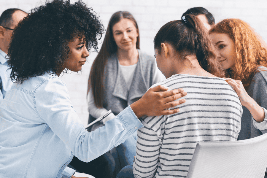 Support group meeting at Axiom Care, where individuals in addiction recovery provide encouragement to a distressed woman. Compassionate peer support is a key part of the healing journey.